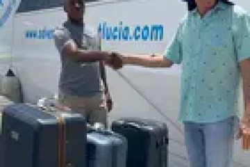 Two people shaking hands beside luggage and a boat on a sunny day.